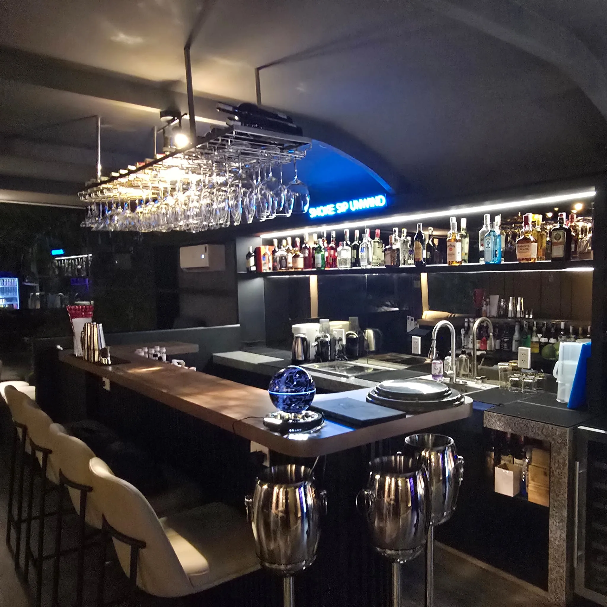 Natasha Noir Lounge bar with hanging glassware and Smoke Sip Unwind neon sign
